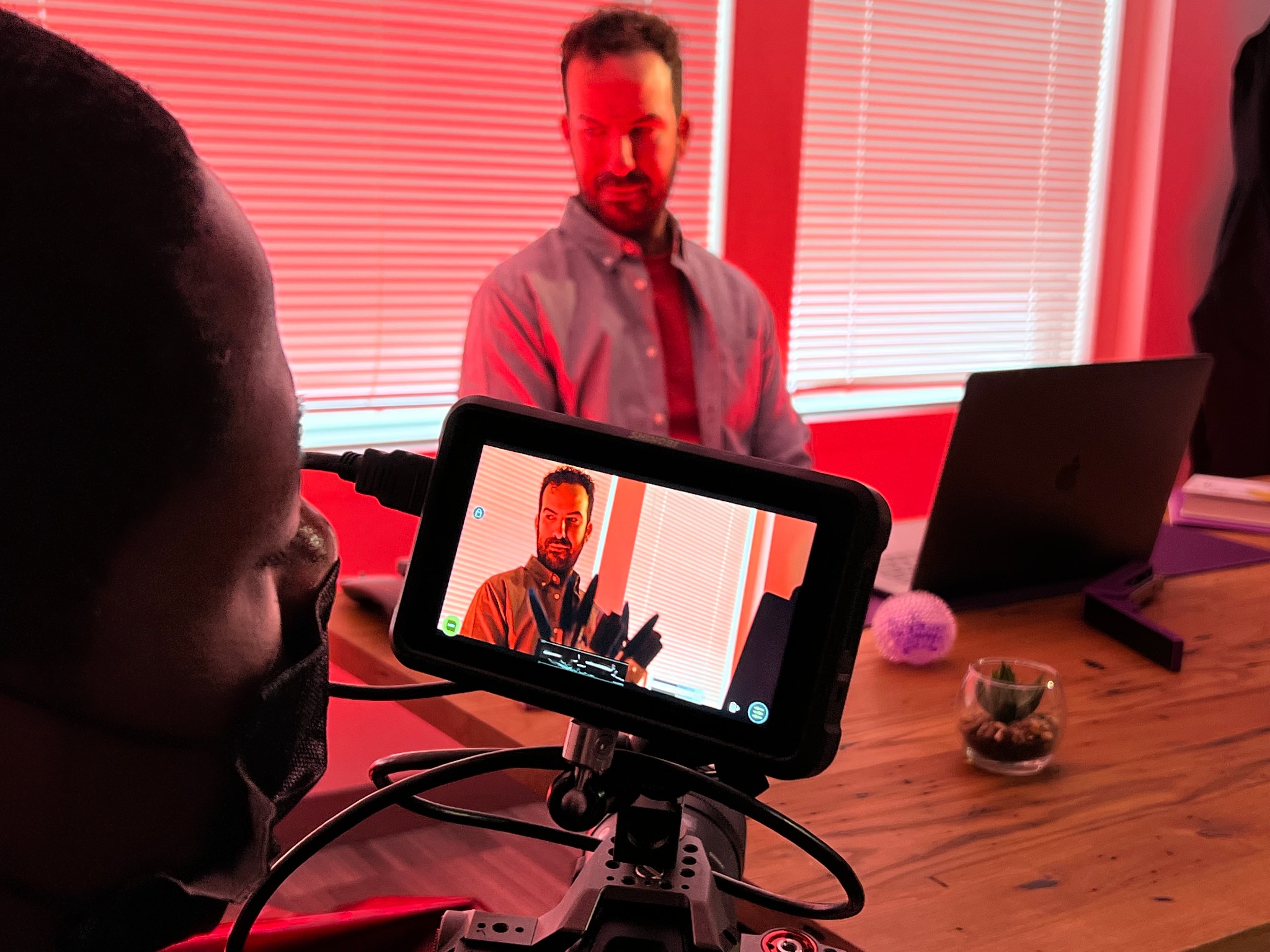 Camera team filming an actor at a desk with dramatic red lighting